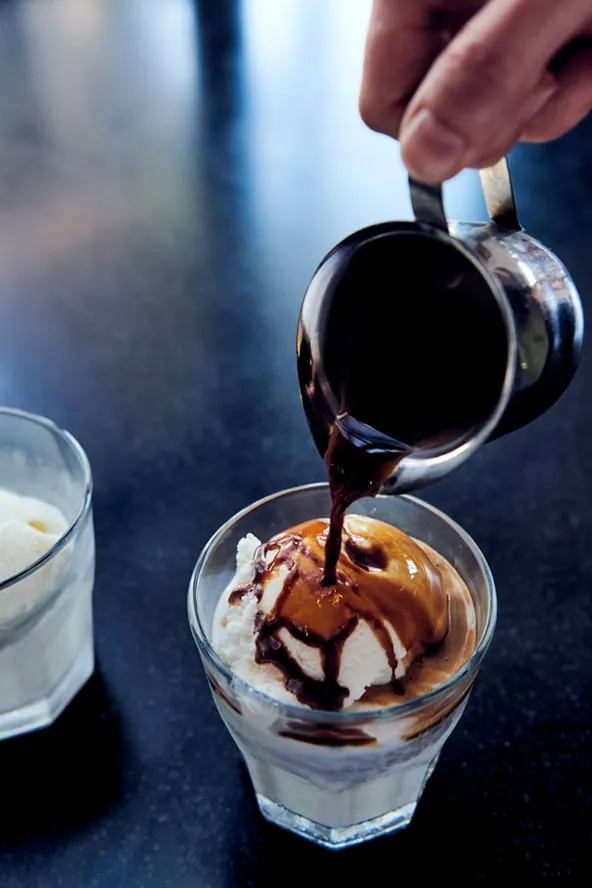 Espresso being poured over gelato in a glass.