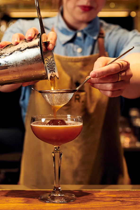 A cocktail being strained into a glass with ice.